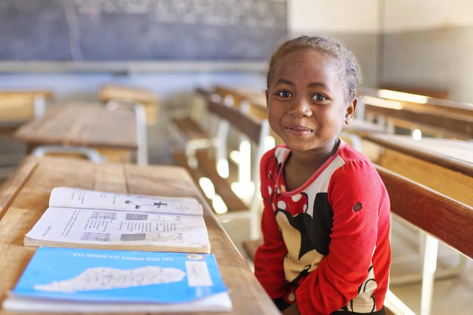 Enfant devat un cahier qui regarde la caméra dans une salle de classe vide