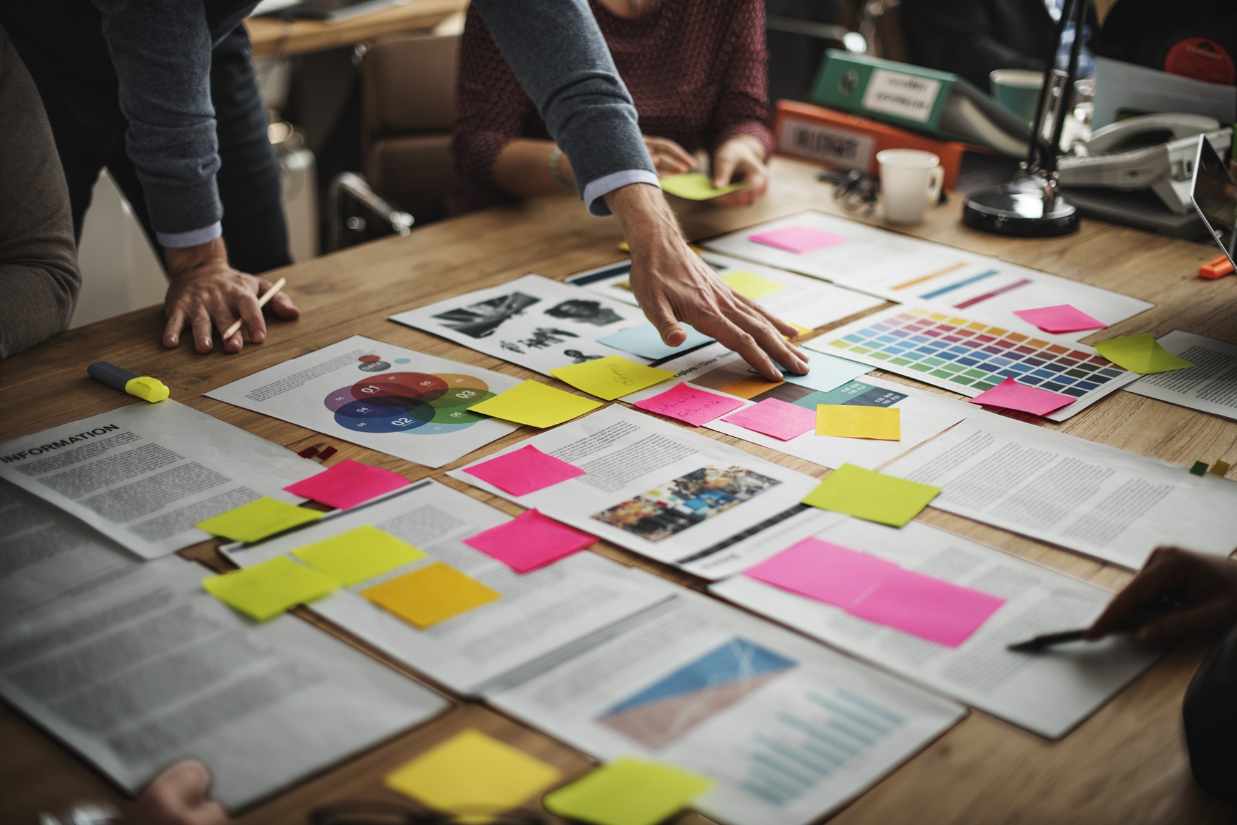Personnes travaillant autour d’une table avec des documents, graphiques et post-it colorés, en pleine séance de brainstorming.