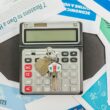 Clé de maison posée sur une calculatrice entourée de documents liés au crédit immobilier et à l’achat d’un logement.