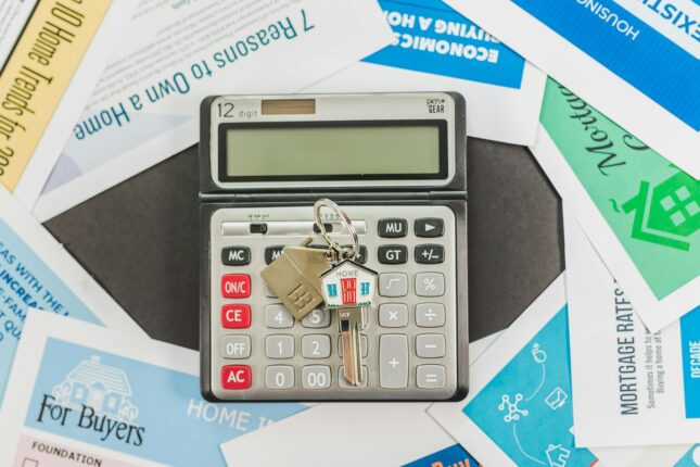 Clé de maison posée sur une calculatrice entourée de documents liés au crédit immobilier et à l’achat d’un logement.