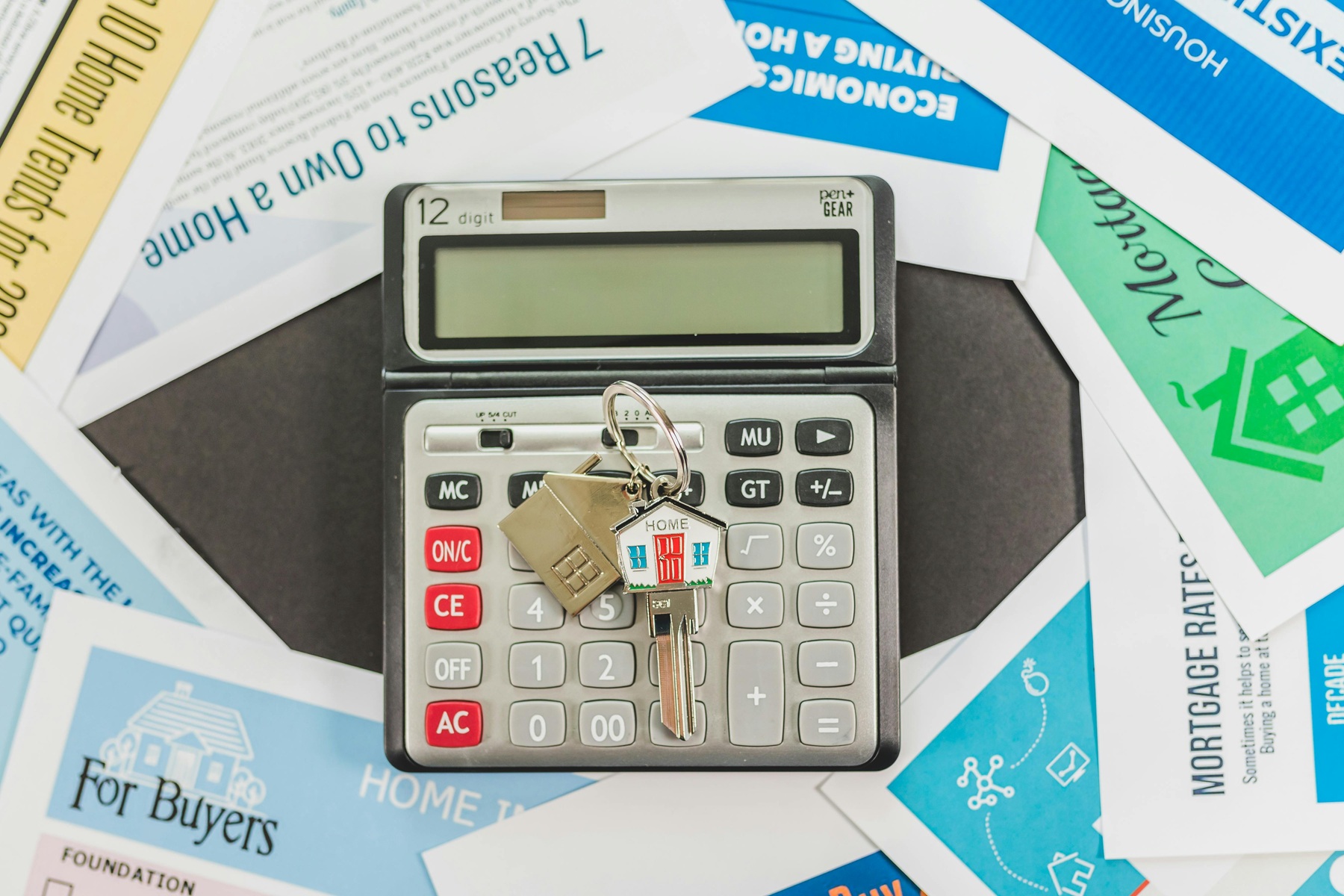 Clé de maison posée sur une calculatrice entourée de documents liés au crédit immobilier et à l’achat d’un logement.