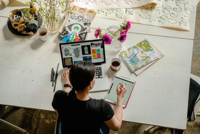 Personne travaillant sur une tablette et un ordinateur avec des supports graphiques sur une table.