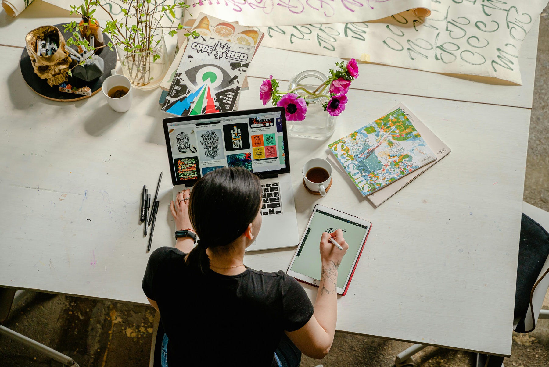 Personne travaillant sur une tablette et un ordinateur avec des supports graphiques sur une table.