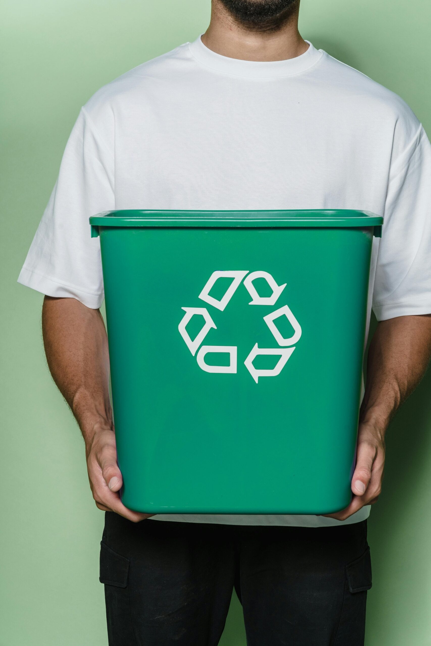 Personne tenant une poubelle verte avec le symbole du recyclage, illustrant la gestion et le tri des déchets.
