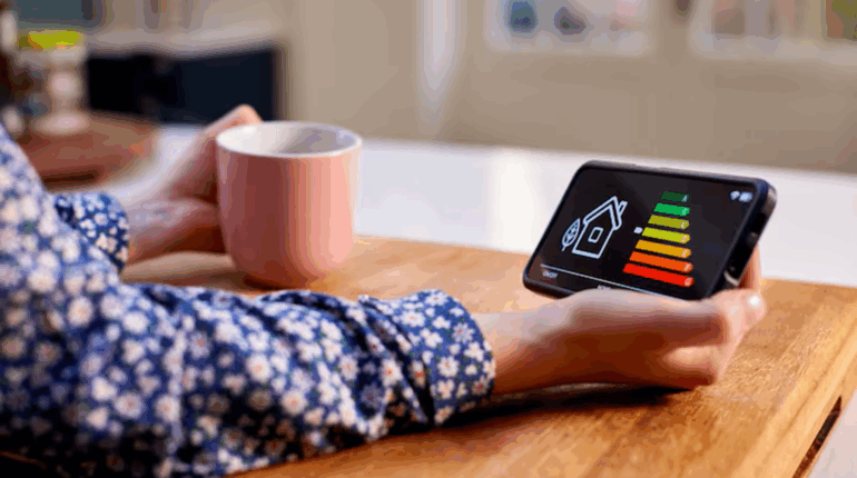 Une personne consulte un diagnostic de performance énergétique (DPE) sur son smartphone tout en tenant une tasse, dans un intérieur lumineux.