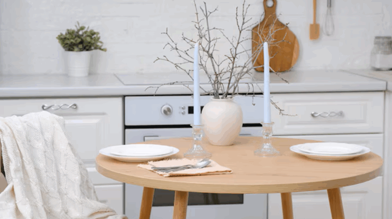 Table ronde dans une cuisine blanche, avec chandeliers, vase décoratif et branches sèches.