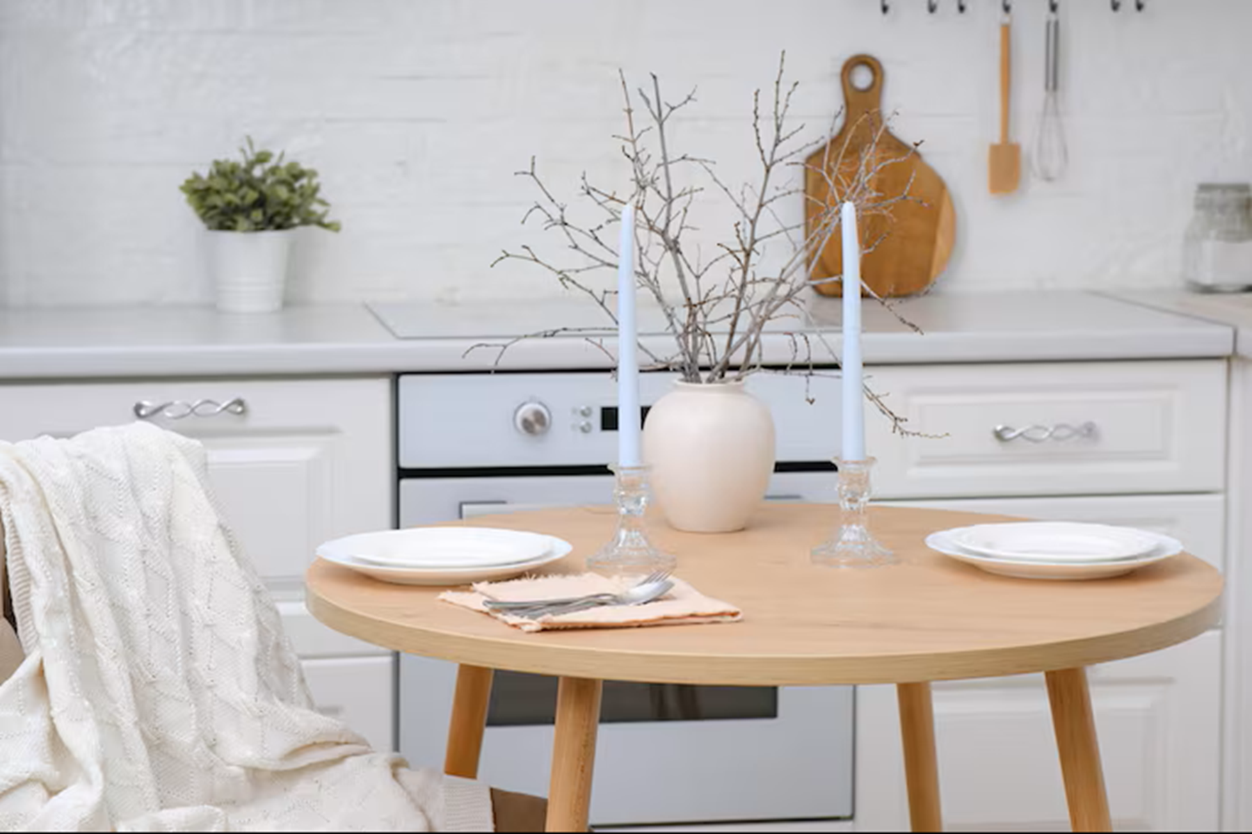 Table ronde dans une cuisine blanche, avec chandeliers, vase décoratif et branches sèches.