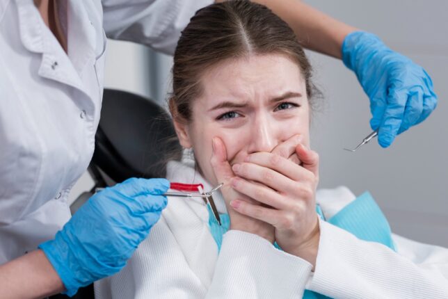 Jeune femme apeurée chez le dentiste, se couvrant la bouche avec les mains.