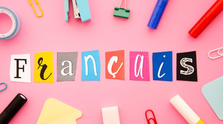 Mot Français écrit avec des lettres colorées découpées sur fond rose, entouré de fournitures scolaires