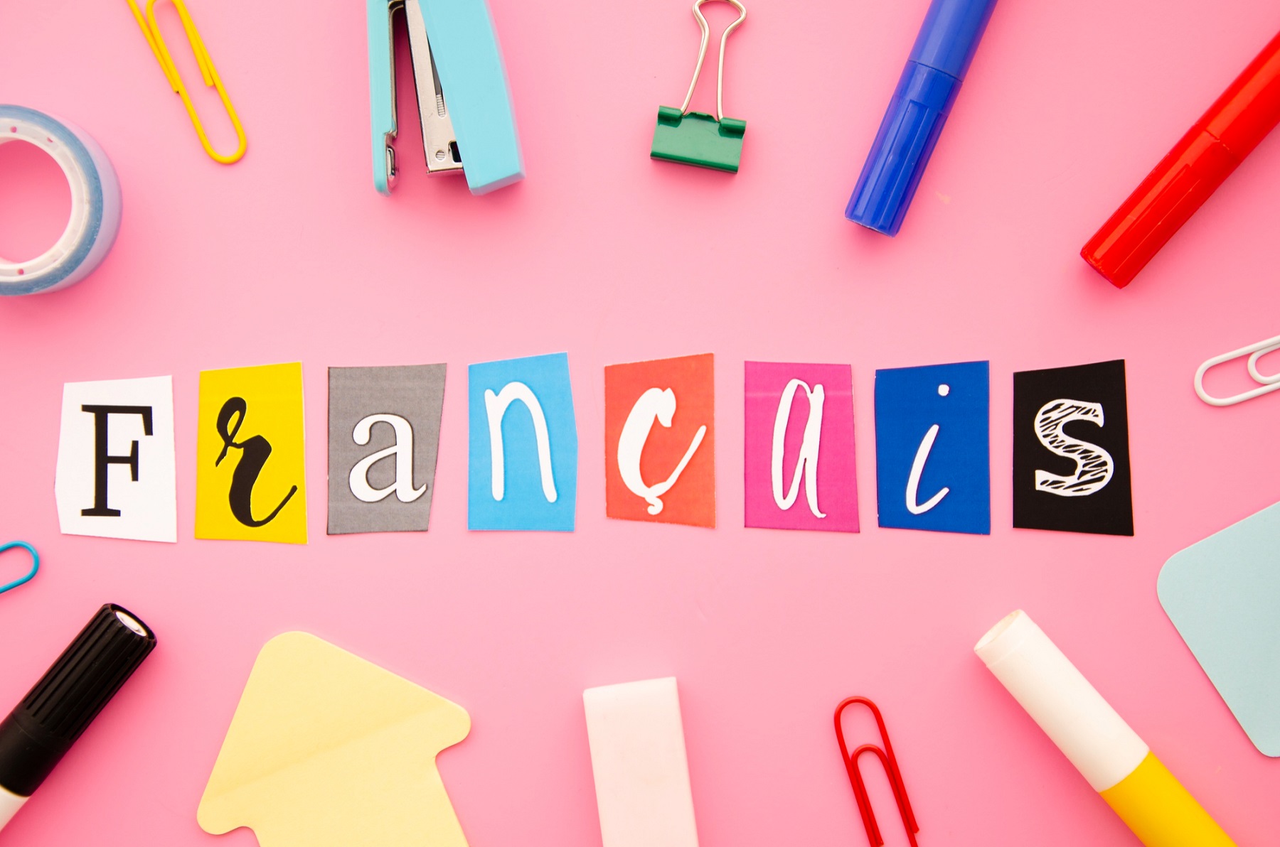 Mot Français écrit avec des lettres colorées découpées sur fond rose, entouré de fournitures scolaires
