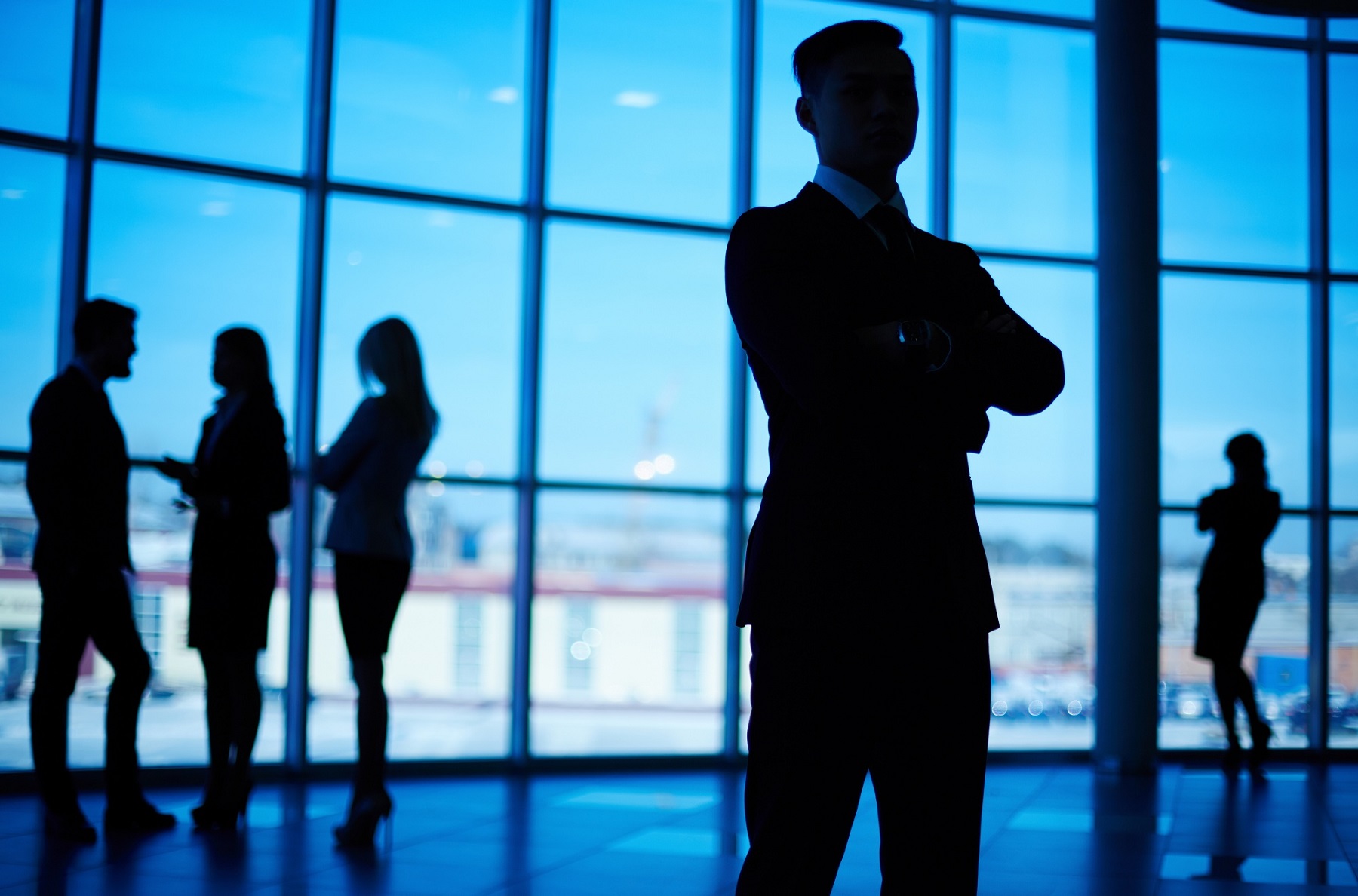 Silhouettes de personnes en costume discutant dans un bureau avec de grandes fenêtres.