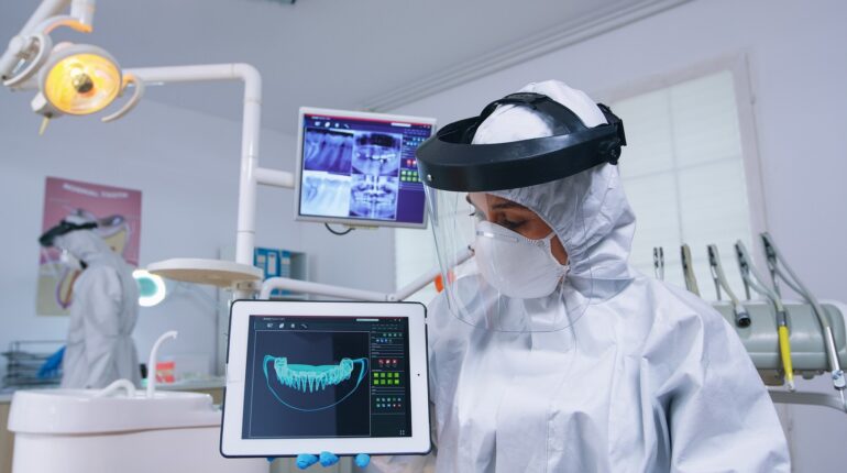 Un dentiste en tenue de protection regarde une image de dents sur une tablette dans un cabinet dentaire