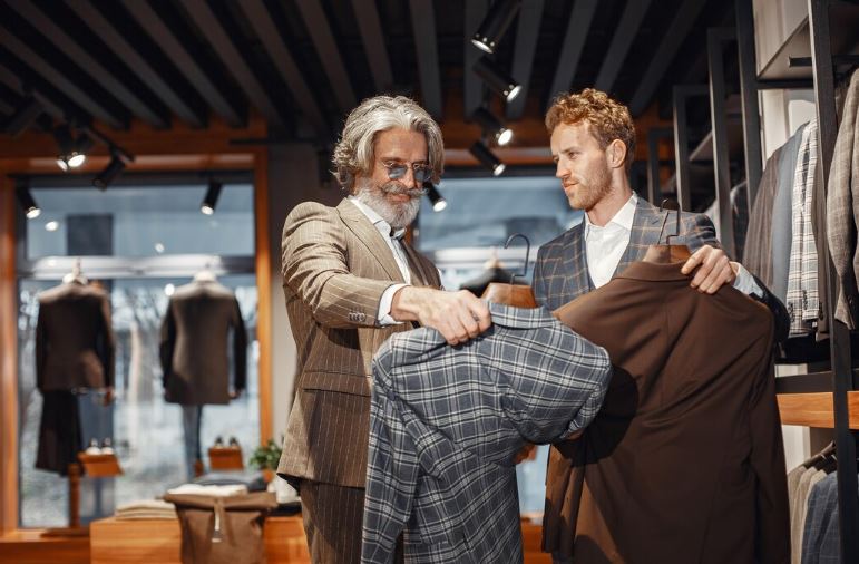 Homme aidant un client senior à choisir un costume dans une boutique de mode masculine.