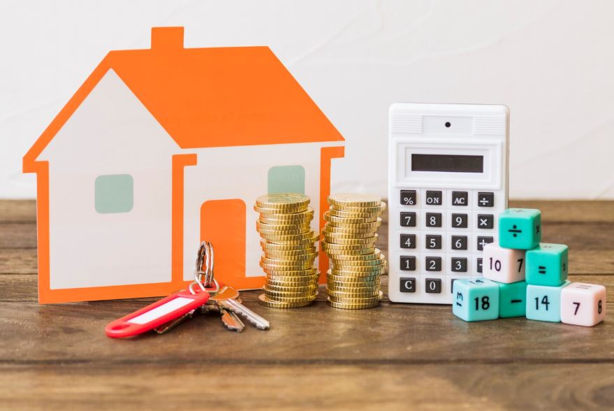 Maison, clé, pièces empilées, calculatrice et blocs de maths sur la table en bois