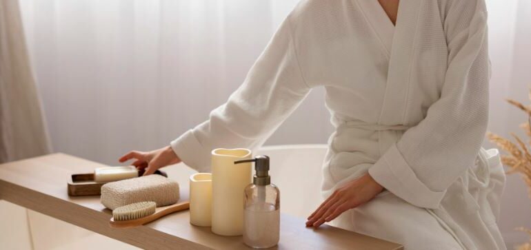 Personne portant un peignoir blanc, assise près d’une table avec des accessoires de spa