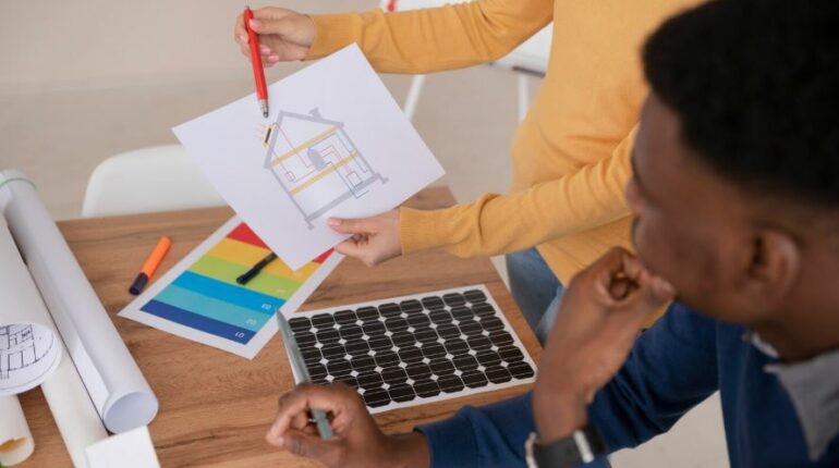 Deux personnes examinent un plan de maison et des outils liés à l’efficacité énergétique sur une table