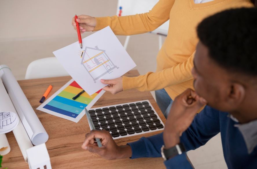 Deux personnes examinent un plan de maison et des outils liés à l’efficacité énergétique sur une table