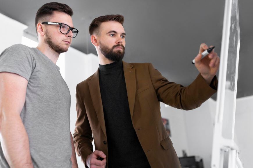 Deux hommes regardent un tableau blanc.