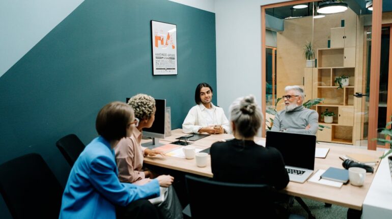 Un manager debout devant une équipe en réunion, échangeant des idées autour d’une table