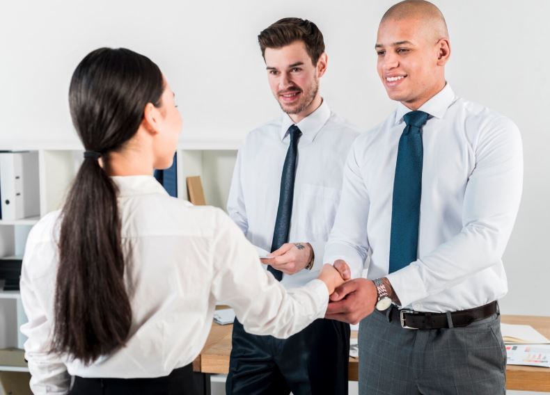 Un échange professionnel souriant entre trois collaborateurs marqué par une poignée de main dans un bureau
