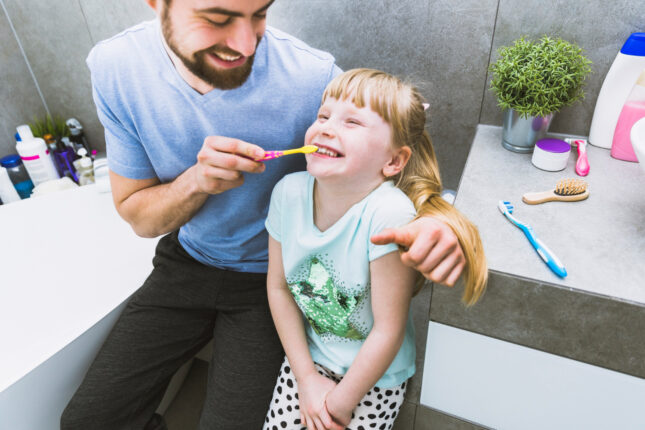 Un père aide sa fille à se brosser les dents dans la salle de bain.