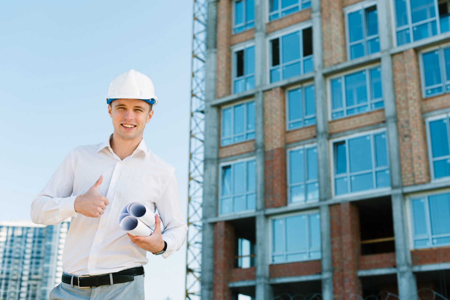 Jeune professionnel du bâtiment faisant un signe de réussite devant un immeuble en chantier.