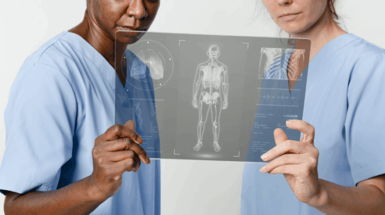 Deux professionnelles de santé en blouse médicale bleue examinent attentivement une tablette transparente futuriste affichant un scan corporel en 3D et des données d'imagerie médicale