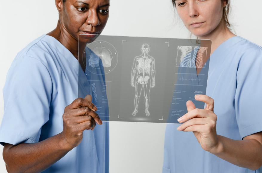 Deux professionnelles de santé en blouse médicale bleue examinent attentivement une tablette transparente futuriste affichant un scan corporel en 3D et des données d'imagerie médicale